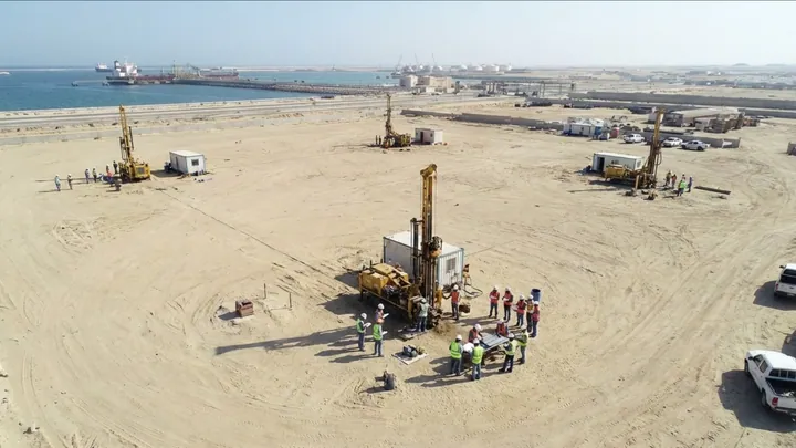 Aerial view of drilling rigs and engineers carrying out soil testing on a coastal site.